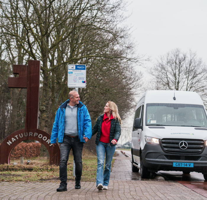 Man en vrouw wandelen op de stoep naast een buurtbus